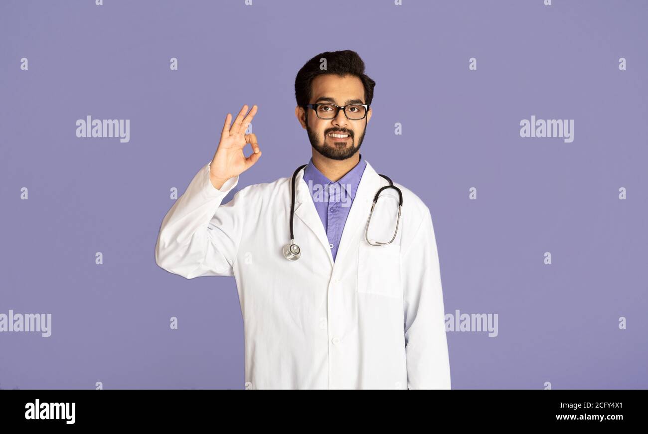Positive Indian doctor showing OK gesture on lilac background Stock Photo -  Alamy