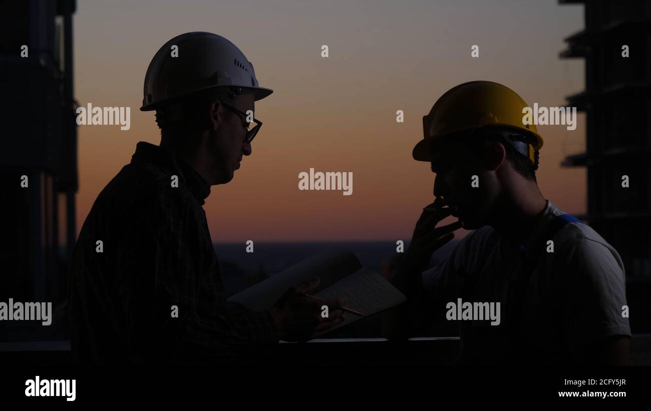 Construction workers having discussion at sunset. One smokes. Stock Photo