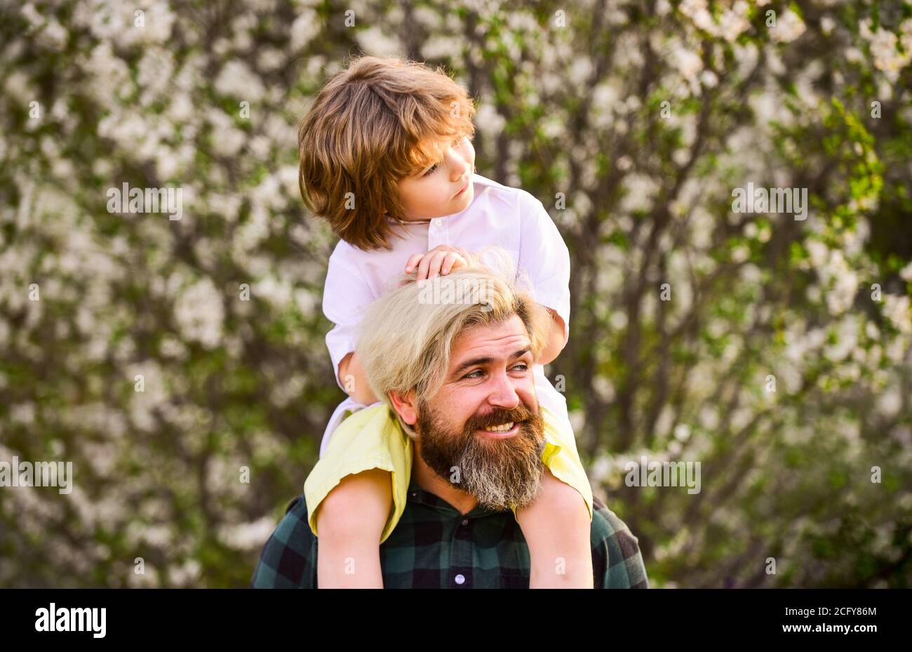 Happy family. Fathers day. Child having fun with dad. Little boy and father in nature background. Springtime. Hipster piggybacking baby. Bearded brutal man good father. Dad and son. Best dad ever. Stock Photo