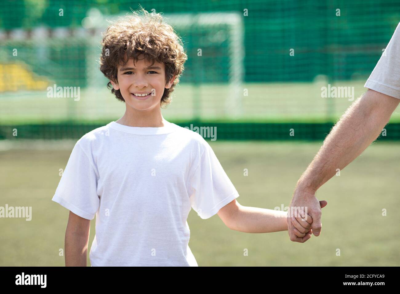 Man holding hand of little boy on football pitch Stock Photo