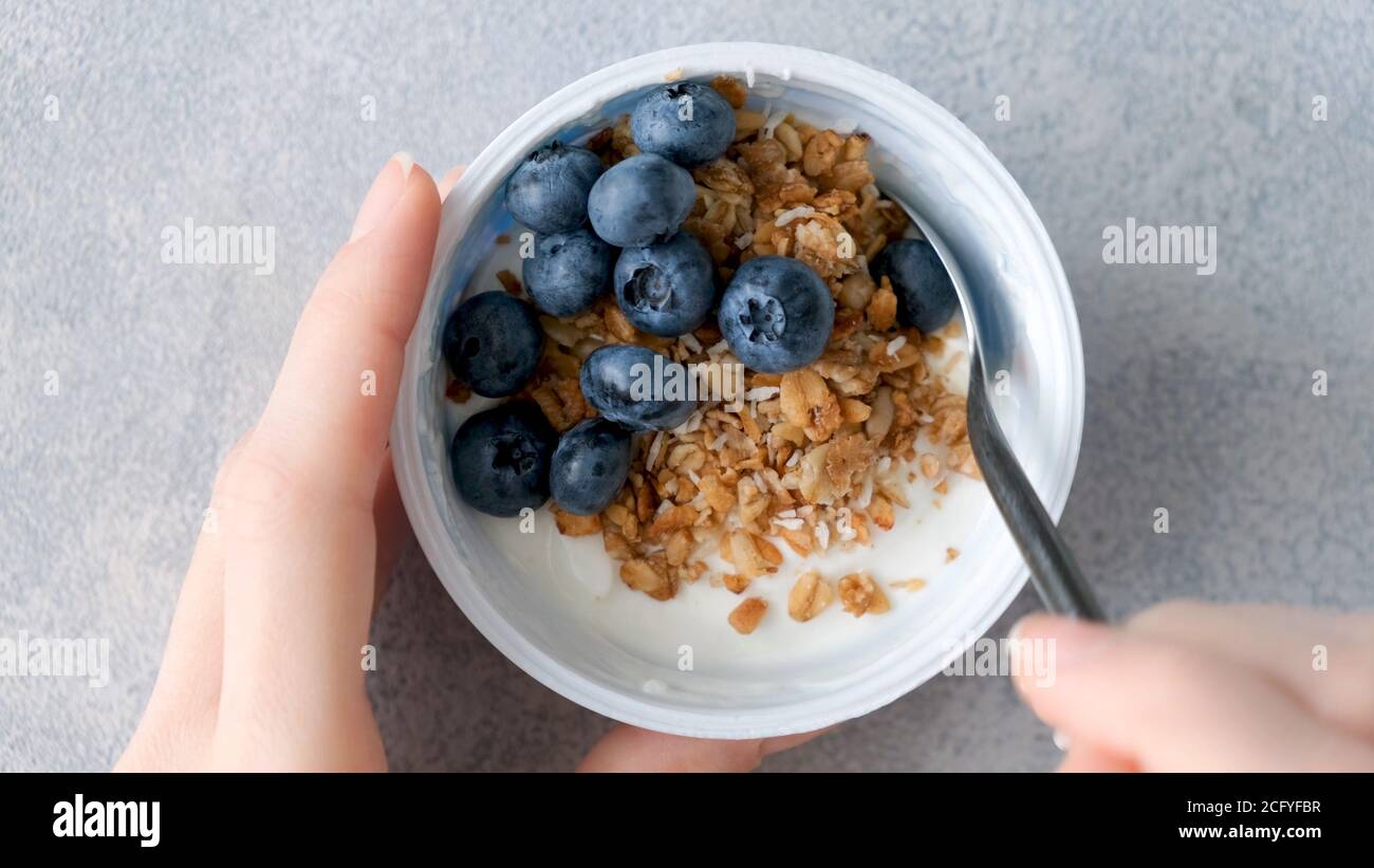 Eating yogurt with granola and blueberries. Female hands holding bowl of greek yogurt with berries and granola. Fitness food, dieting, clean eating co Stock Photo