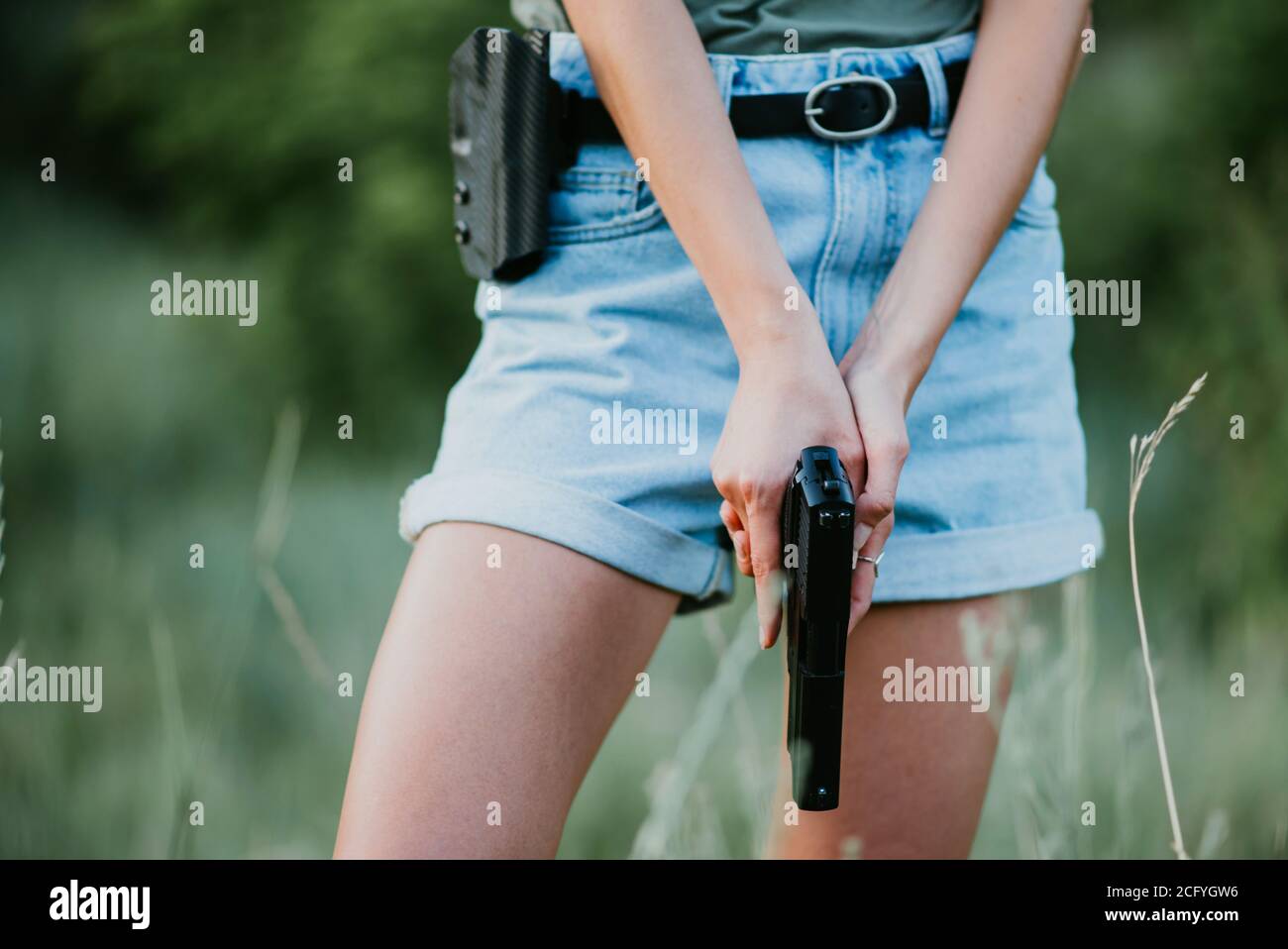 girl in denim shorts and with a gun in his hand posing in the field. Stock Photo