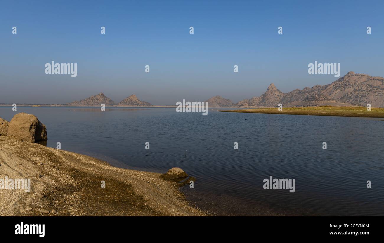 Landscape of Jawai dam with water, clear blue sky and Aravalli mountain ranges with its reflection in water at Jawai in Rajasthan India Stock Photo