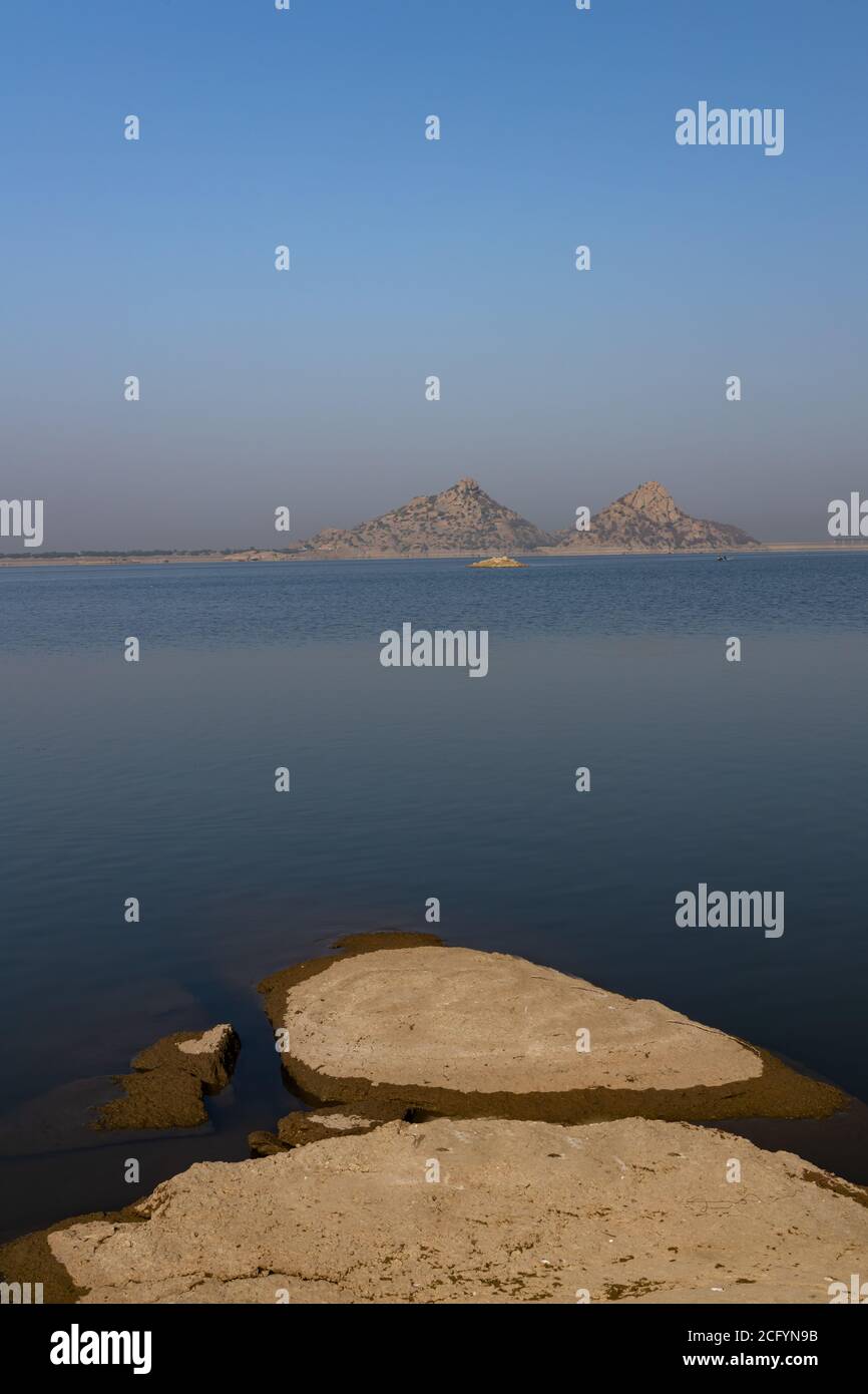 Landscape of Jawai dam with water, clear blue sky and Aravalli mountain ranges with its reflection in water at Jawai in Rajasthan India Stock Photo