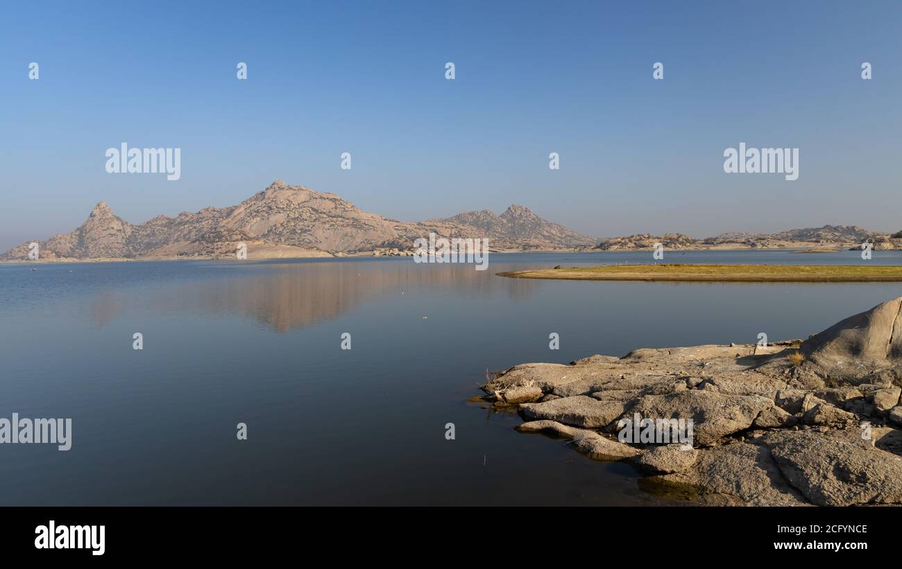 Landscape of Jawai dam with water, clear blue sky and Aravalli mountain ranges with its reflection in water at Jawai in Rajasthan India Stock Photo