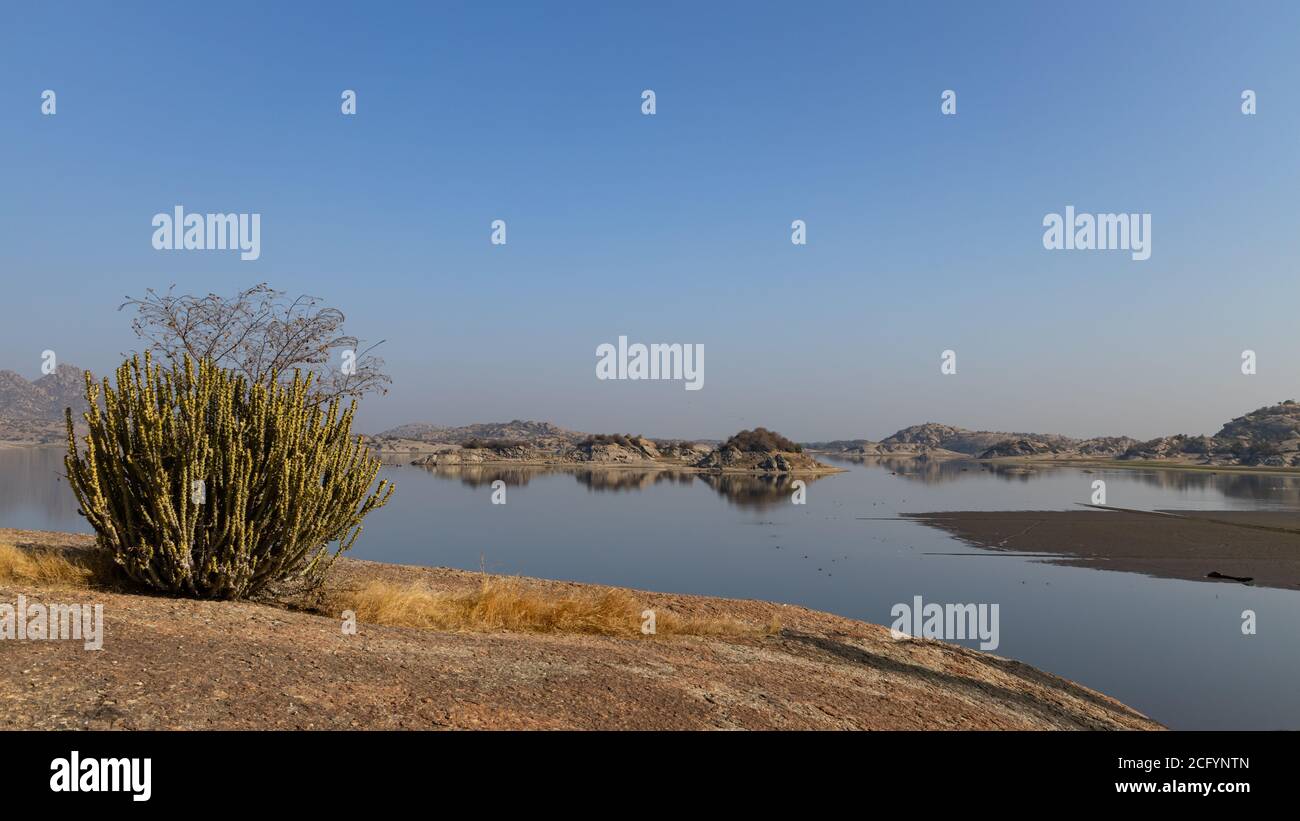 Landscape of Jawai dam with water, clear blue sky and Aravalli mountain ranges with its reflection in water at Jawai in Rajasthan India Stock Photo