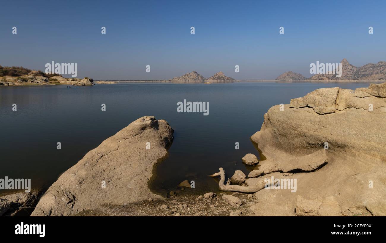 Landscape of Jawai dam with water, clear blue sky and Aravalli mountain ranges with its reflection in water at Jawai in Rajasthan India Stock Photo