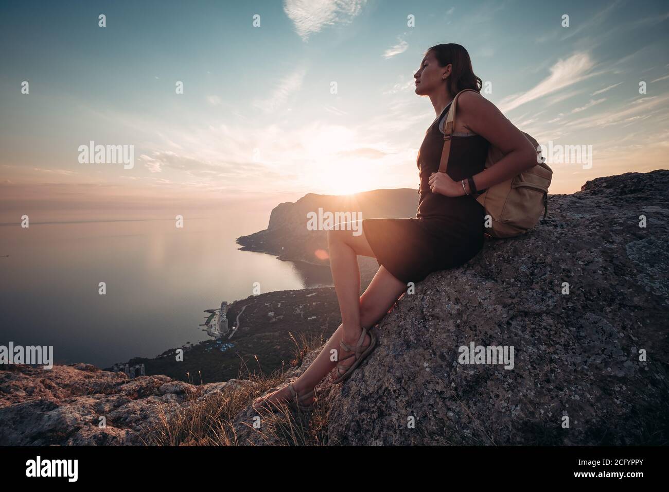A girl sits on the edge of the cliff and looking at the sun sea and ...