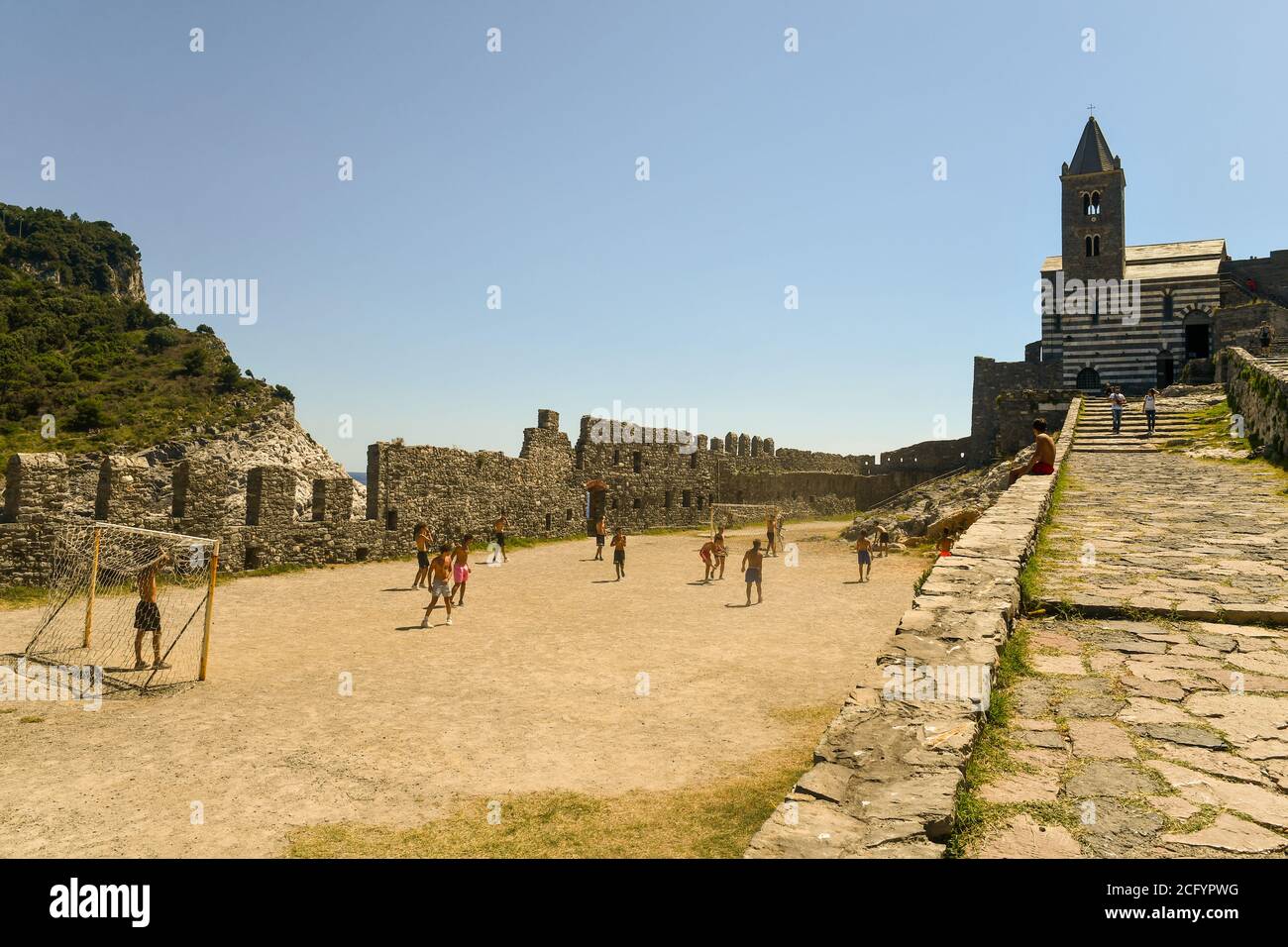 A group of boys playing football in the churchyard of the famous gothic Church of Saint Peter on a summer day, Porto Venere, La Spezia, Liguria, Italy Stock Photo