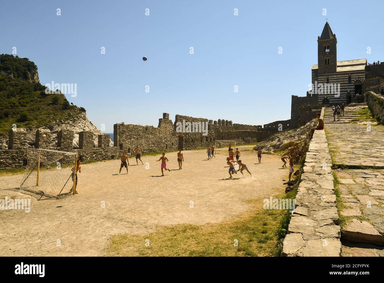 A group of boys playing football in the churchyard of the famous gothic Church of Saint Peter on a summer day, Porto Venere, La Spezia, Liguria, Italy Stock Photo