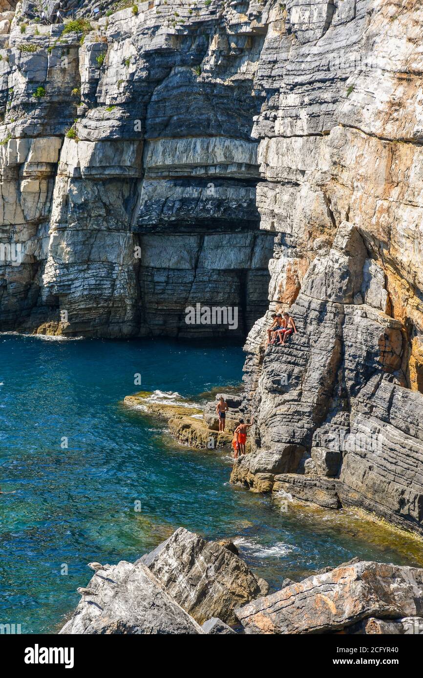A group of teenagers on the rocks next to the Lord Byron's Grotto in a sunny summer day, Porto Venere, La Spezia, Liguria, Italy Stock Photo