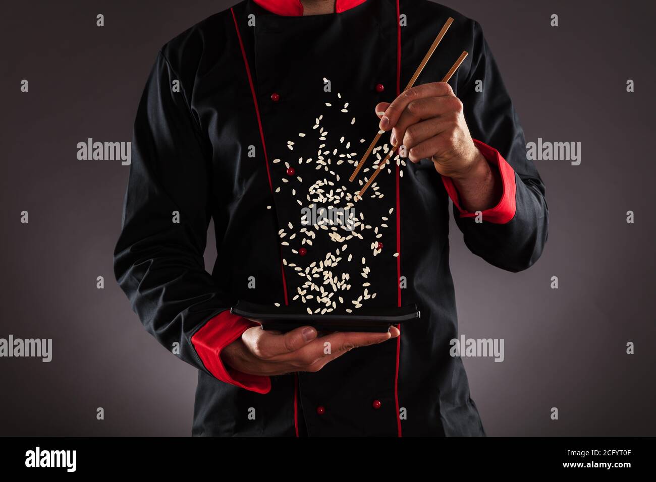Closeup of master chef holding wooden chopsticks with flying rice. Concept of food preparation, ready for product placement. Stock Photo