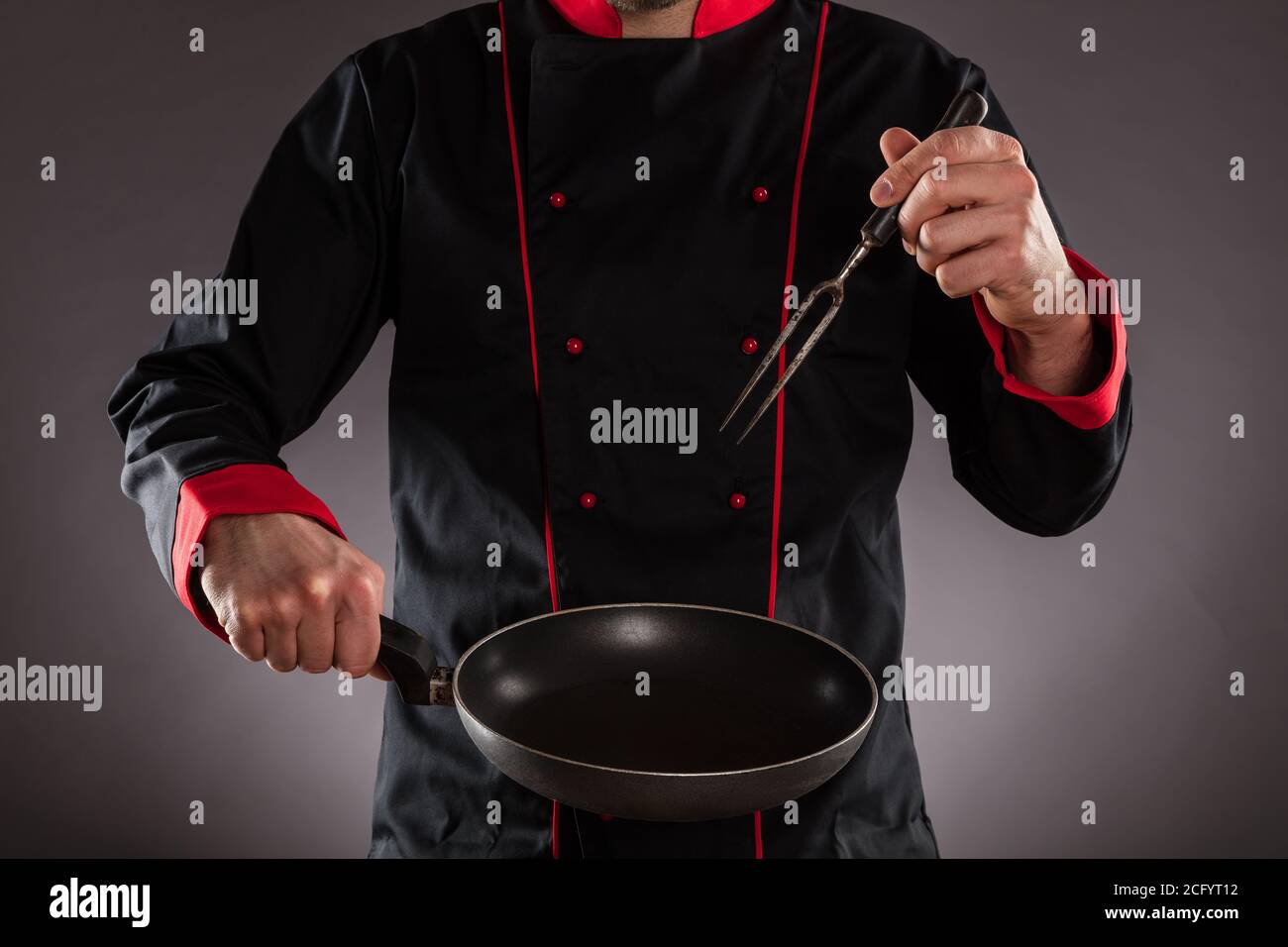 Closeup of master chef holding empty frying pan and fork. Concept of food preparation, ready for product placement. Stock Photo