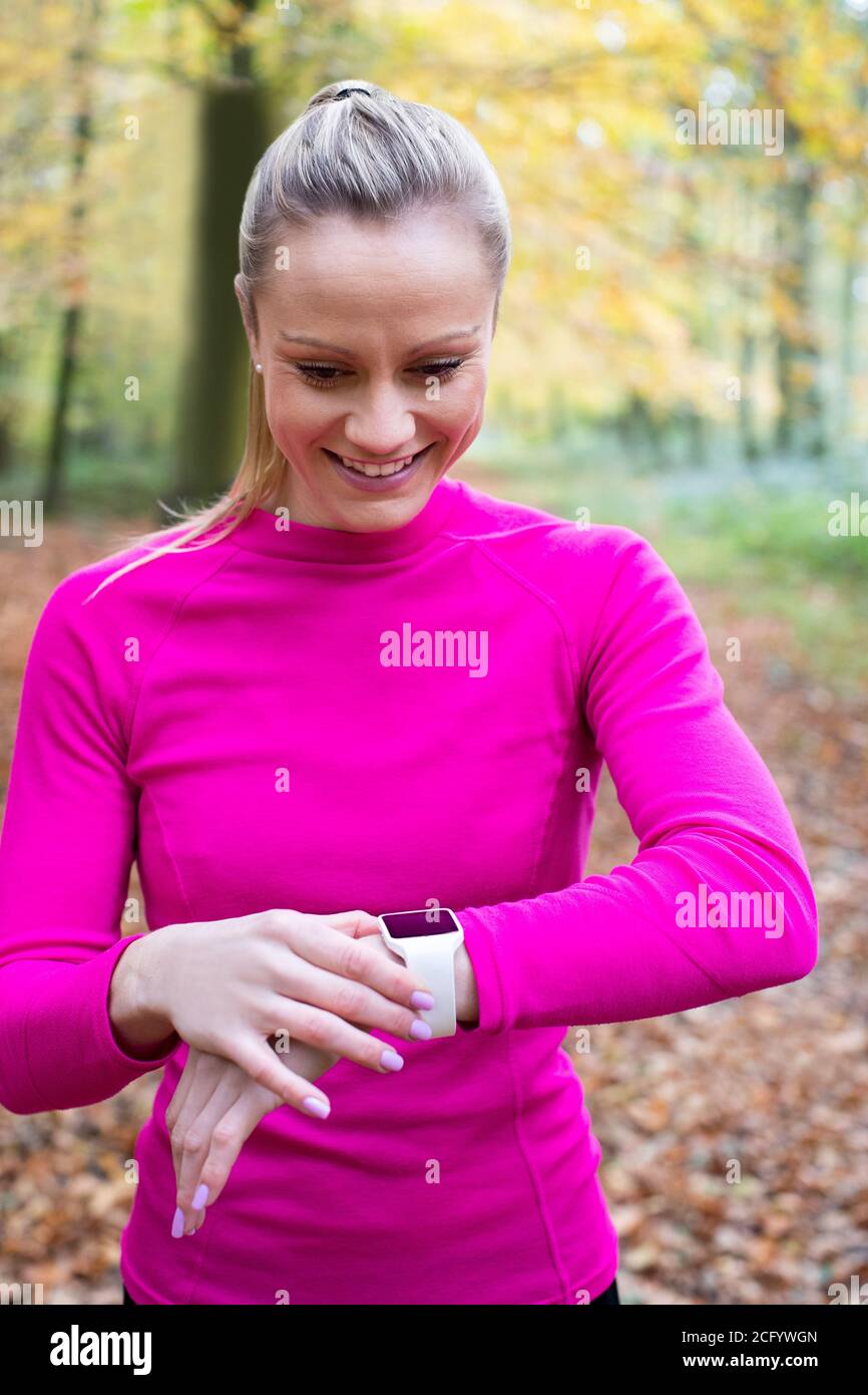 Woman Exercising In Autumn Woodland Looking At Activity Tracker On Smart Watch Stock Photo