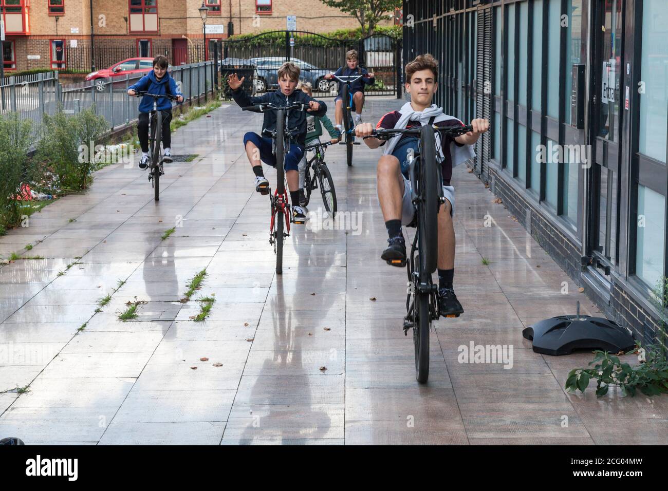 A group of young boys showing how to do wheelies on their bikes in
