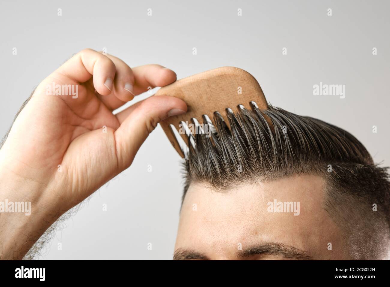 Close up man brushing his hair with wooden comb on the grey background.  Treatment against hair lost and dandruff concept. Cosmetic products for men  Stock Photo - Alamy