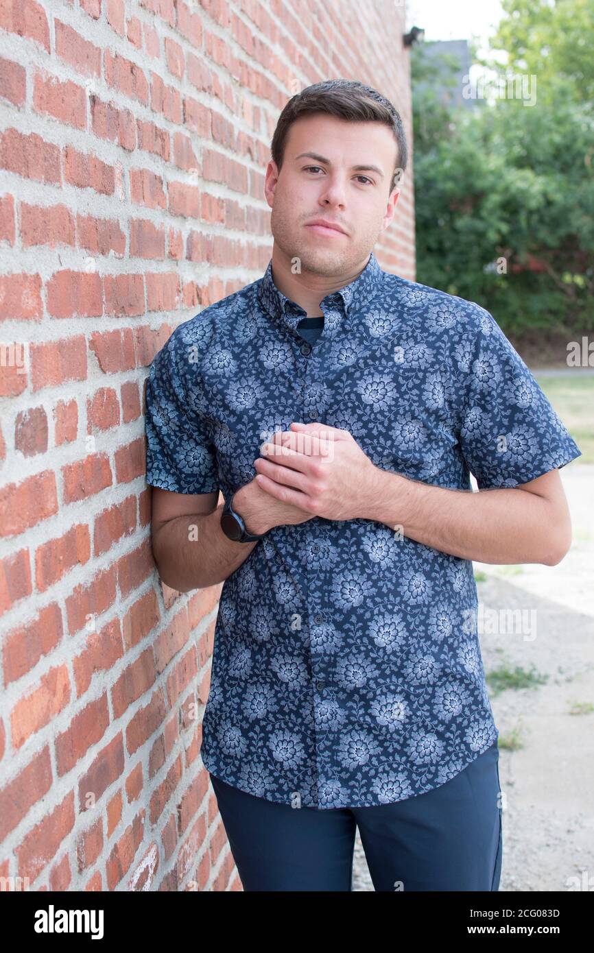 A Portrait of a man in a blue button down shirt against a brick wall Stock Photo