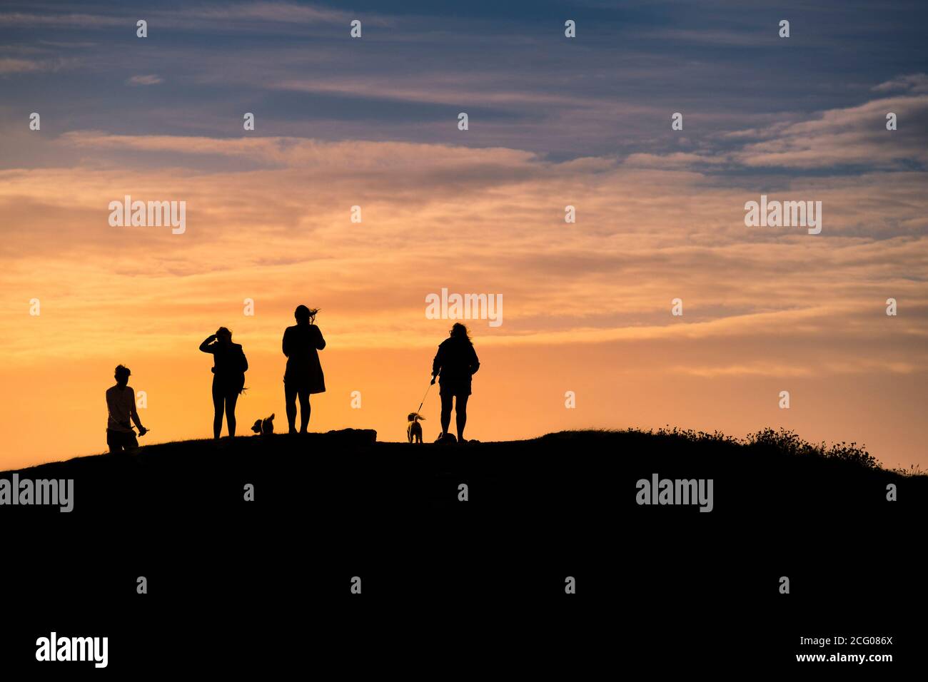 Dog walkers standing on Pentire Point East and silhouetted by a spectacular sunset in Newquay in Cornwall. Stock Photo