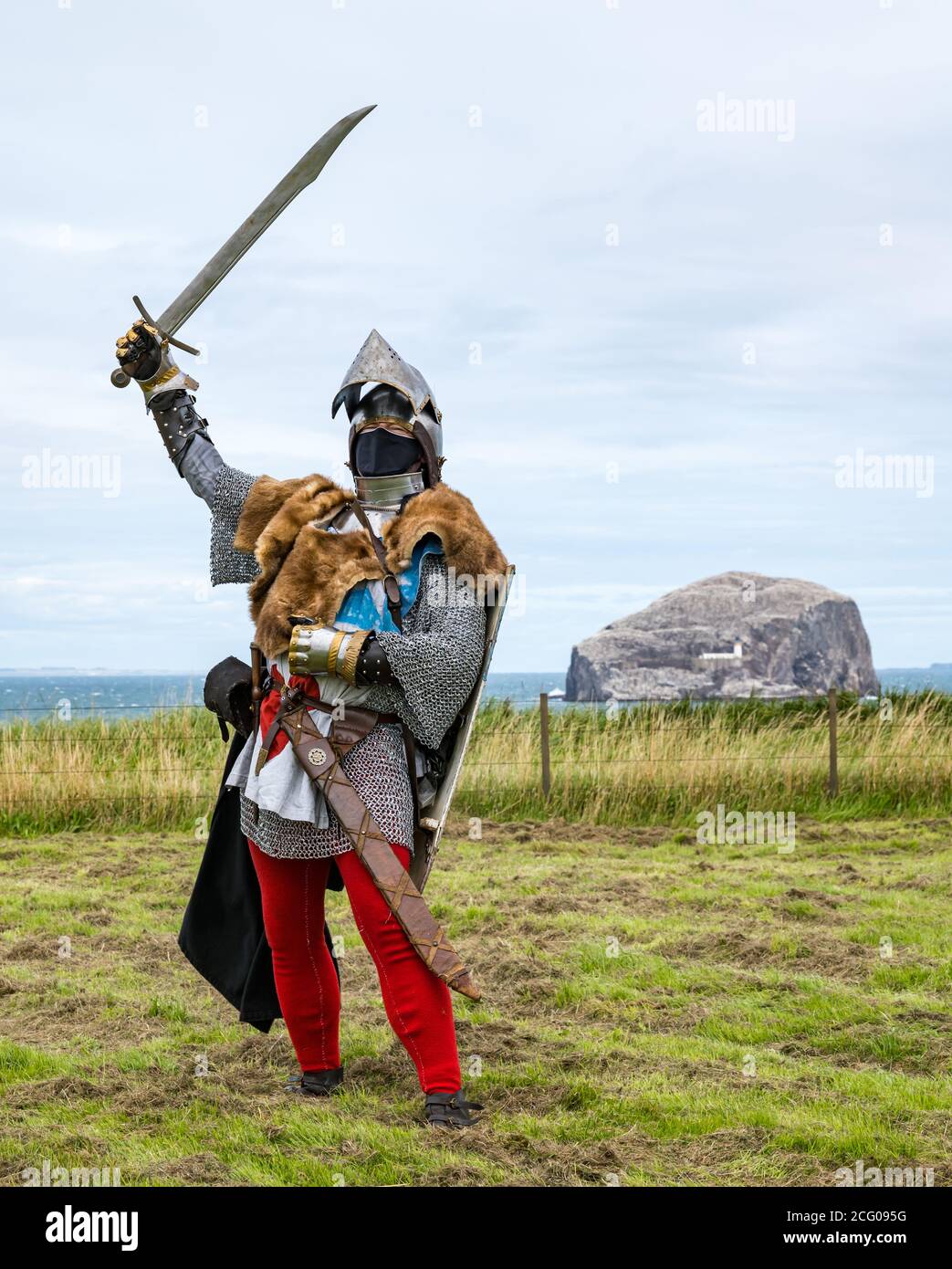 Medieval knight with sword & helmet wearing face mask with view of Bass Rock, Tantallon Castle, East Lothian, Scotland, UK Stock Photo