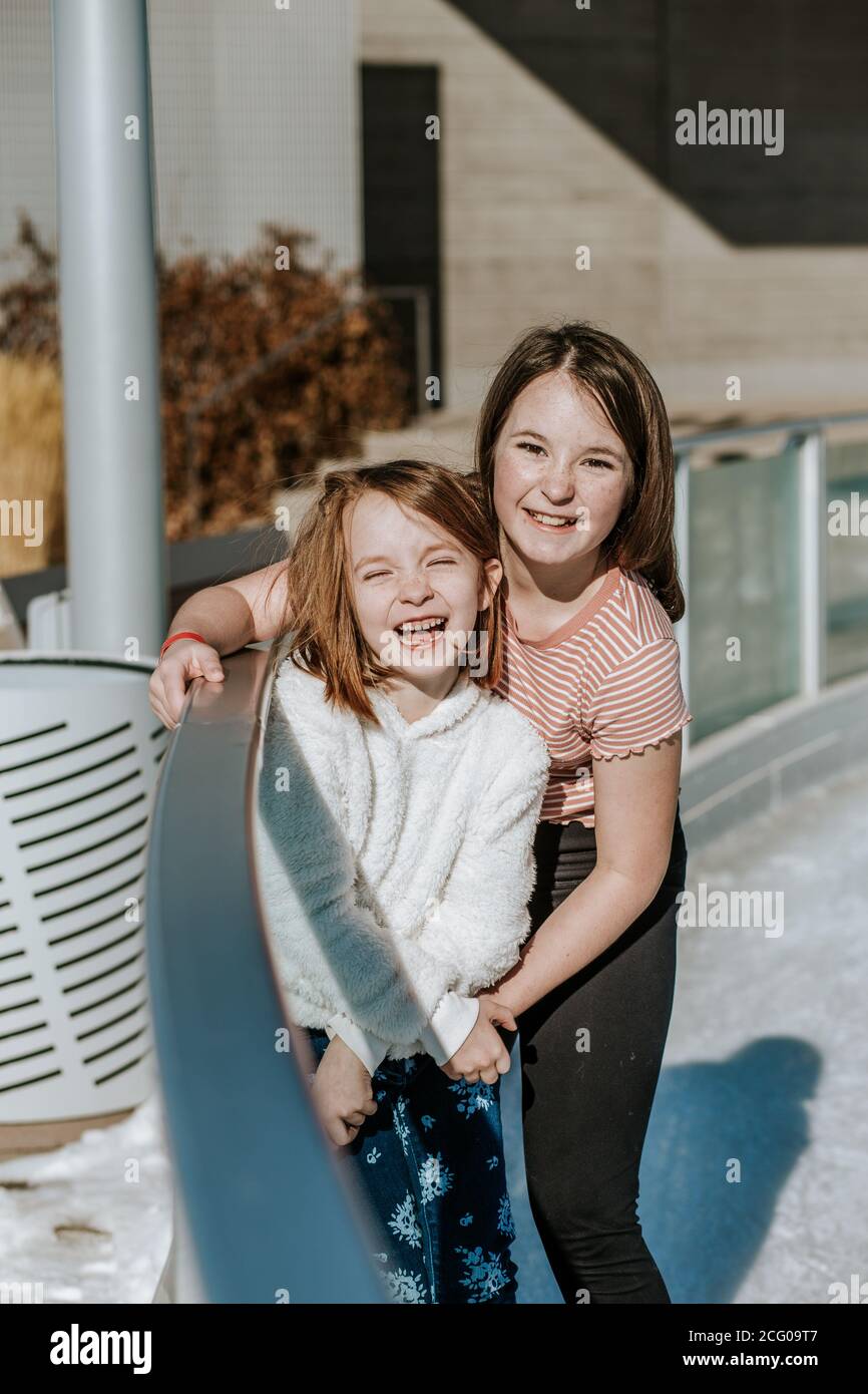 Happy young girls hugging on the side of ice skating rink Stock Photo