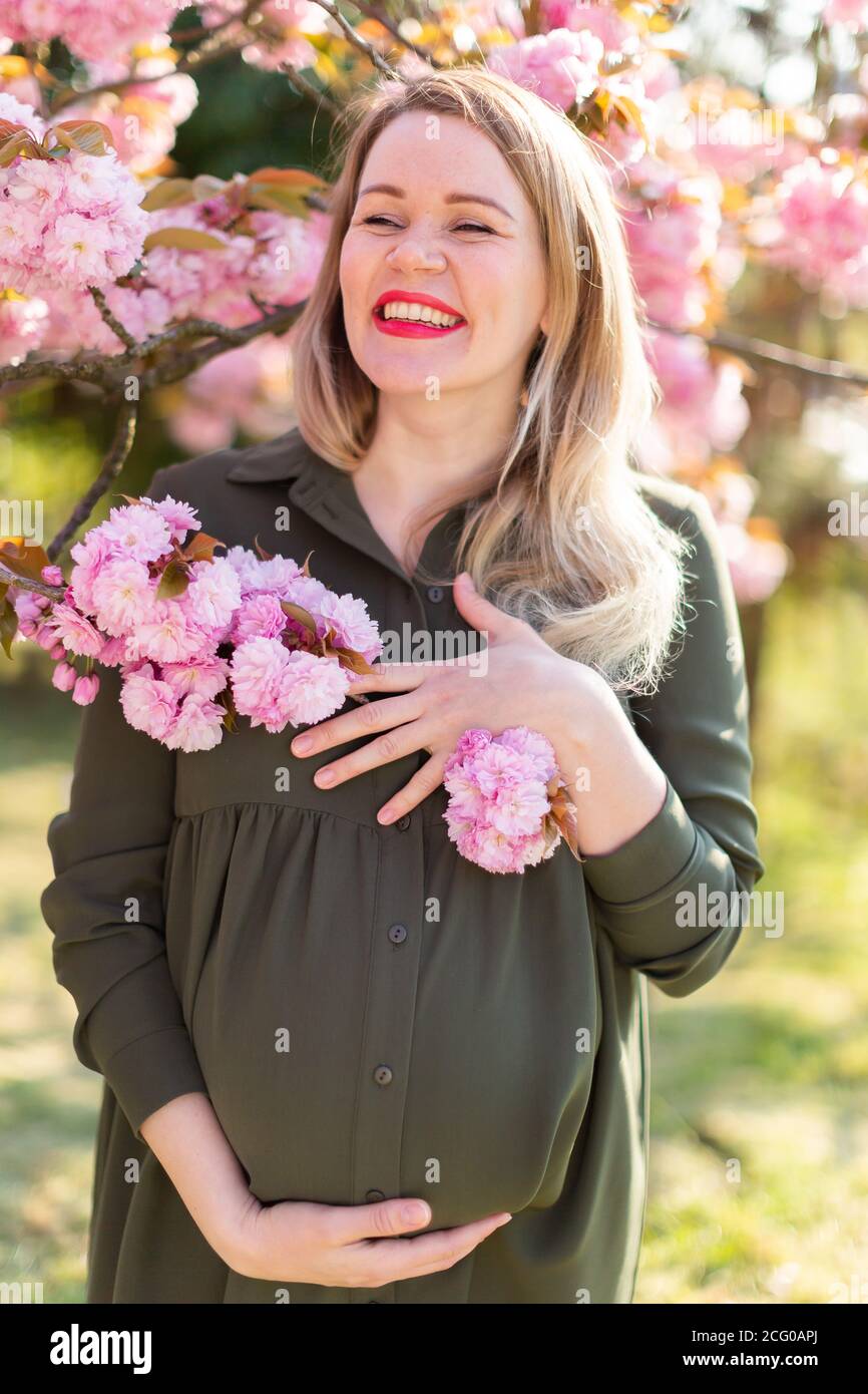 Gentle pregnant woman in the park at spring with cherry blossom trees ...