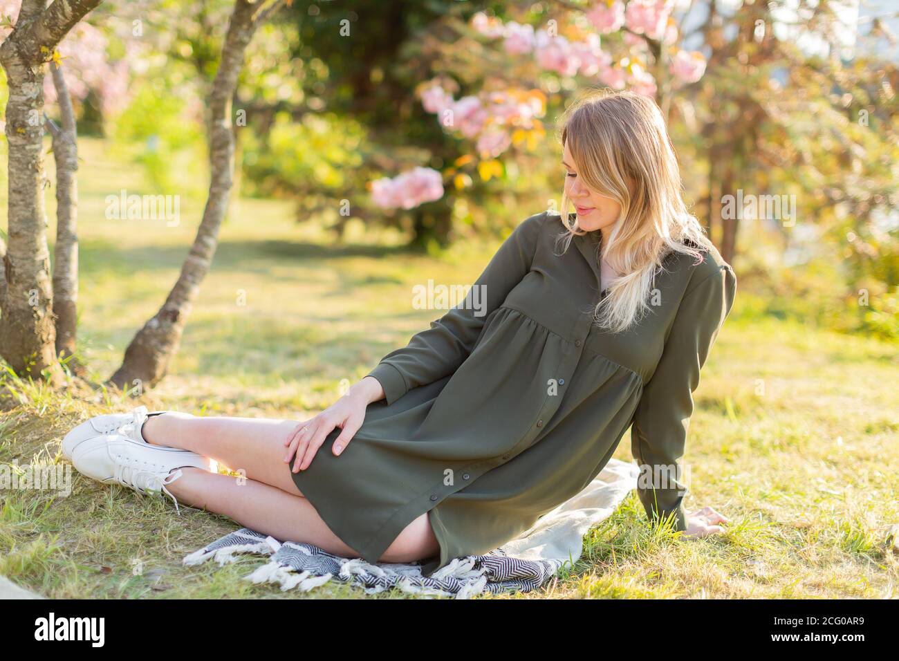 Gentle pregnant woman in the park at spring with cherry blossom trees ...