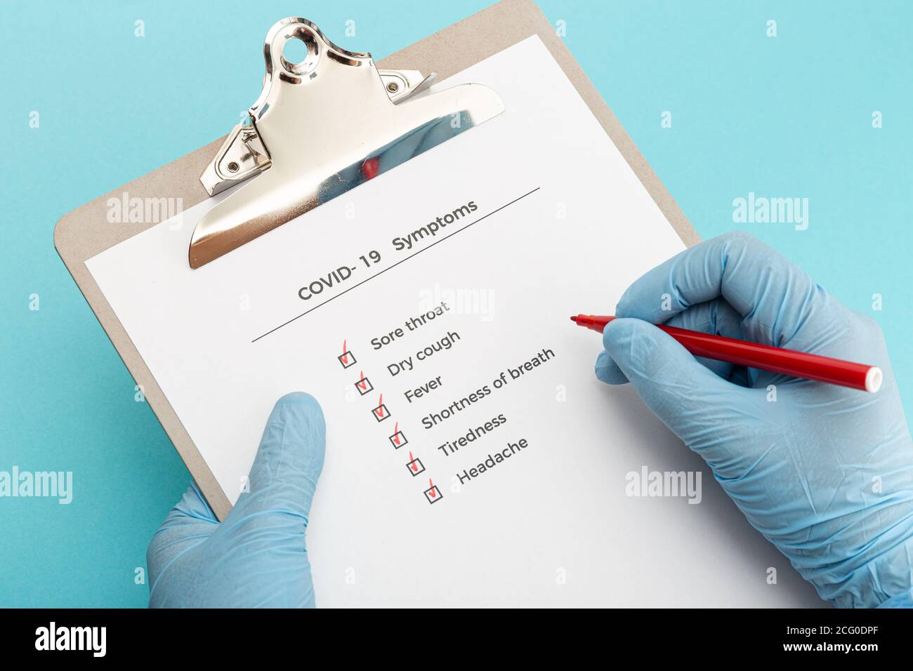 Hands wearing protectives gloves holding a Checklist On Clipboard with COVID-19 symptoms Stock Photo