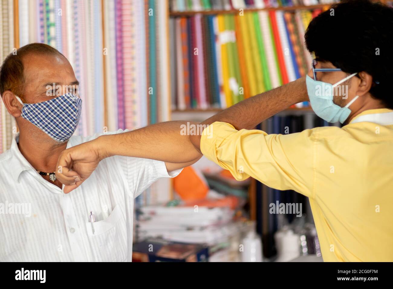 Shopkeeper greeting customer with elbow bump at cloth store - concept of people avoiding hand shakes at business places to stop spreading coronavirus Stock Photo