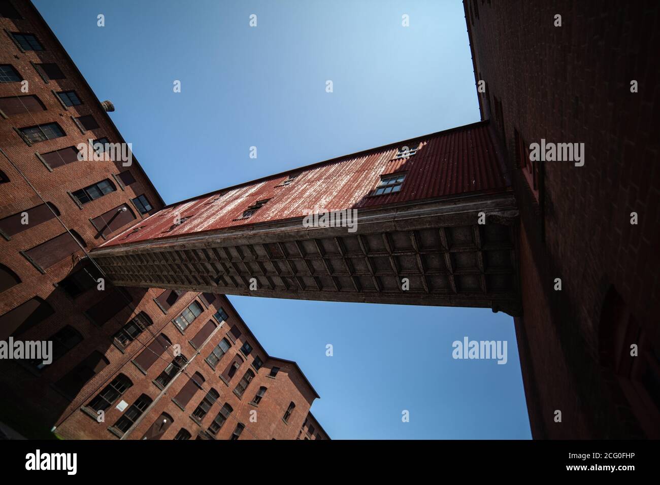 The connection or walkway between two redbrick industrial buildings with nailed up windows - bottom view, and blue clear skies in the background Stock Photo