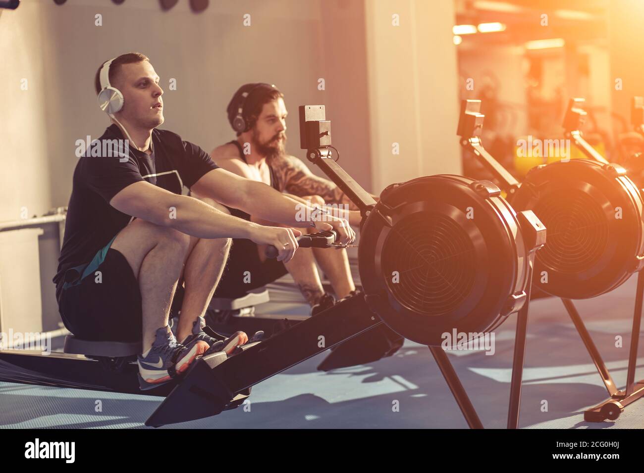 Happy friends training on rowing machine in gym Stock Photo