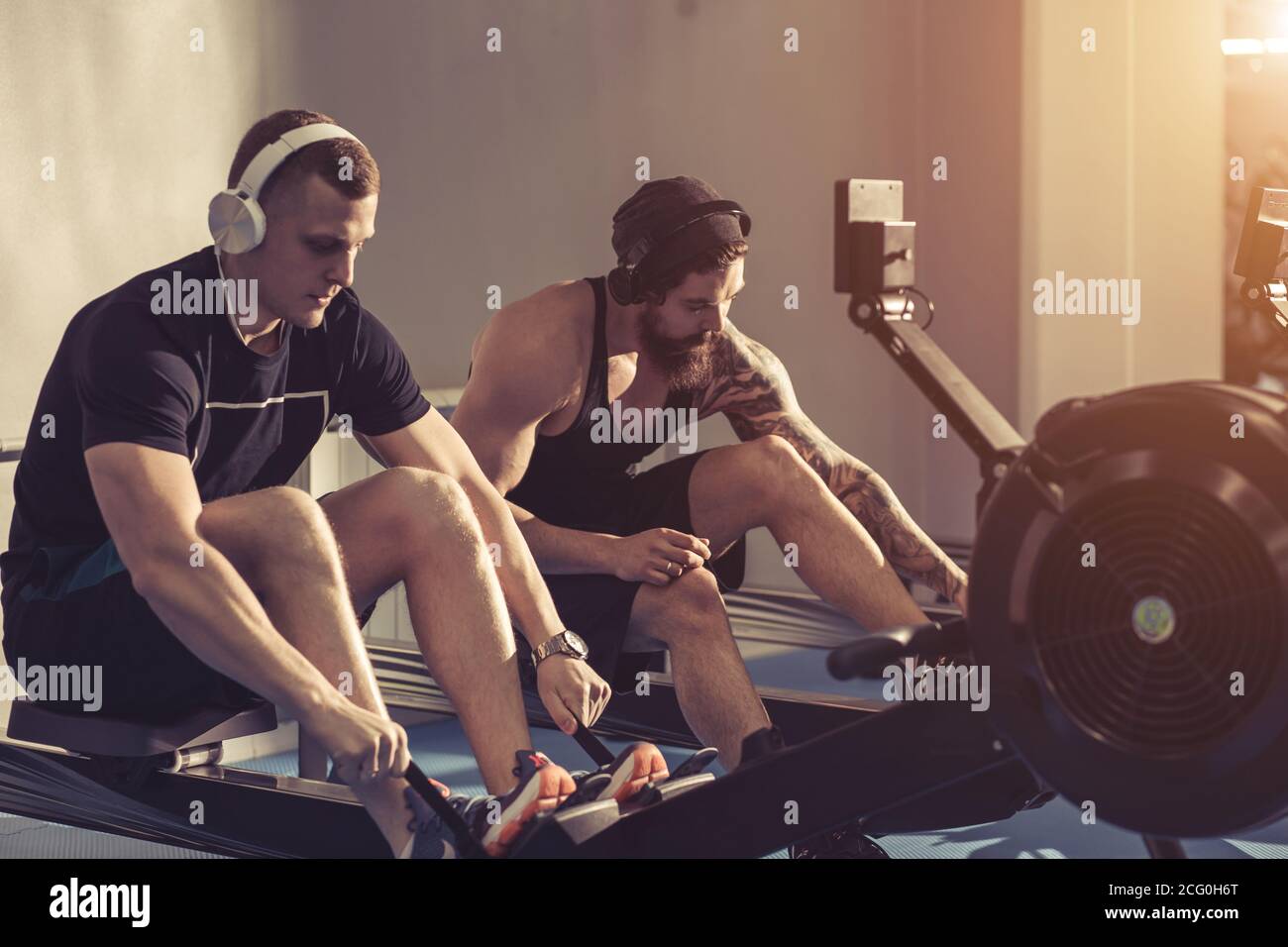 Side view of man and woman doing exercises with rowing machine at gym. Stock Photo