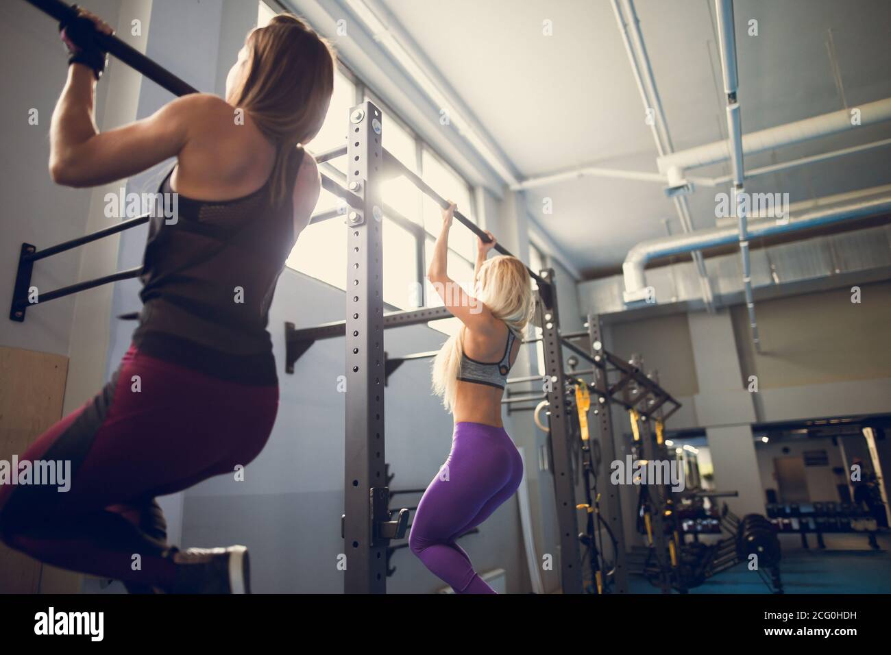 Group of attractive young male and female adults doing pull ups on bar in cross fit training gym with brick walls and black mats Stock Photo