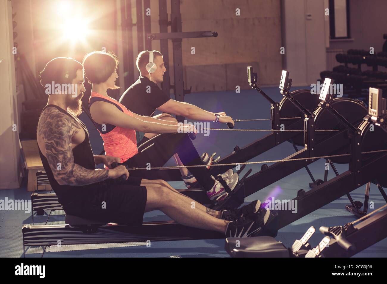 Happy friends training on rowing machine in gym Stock Photo