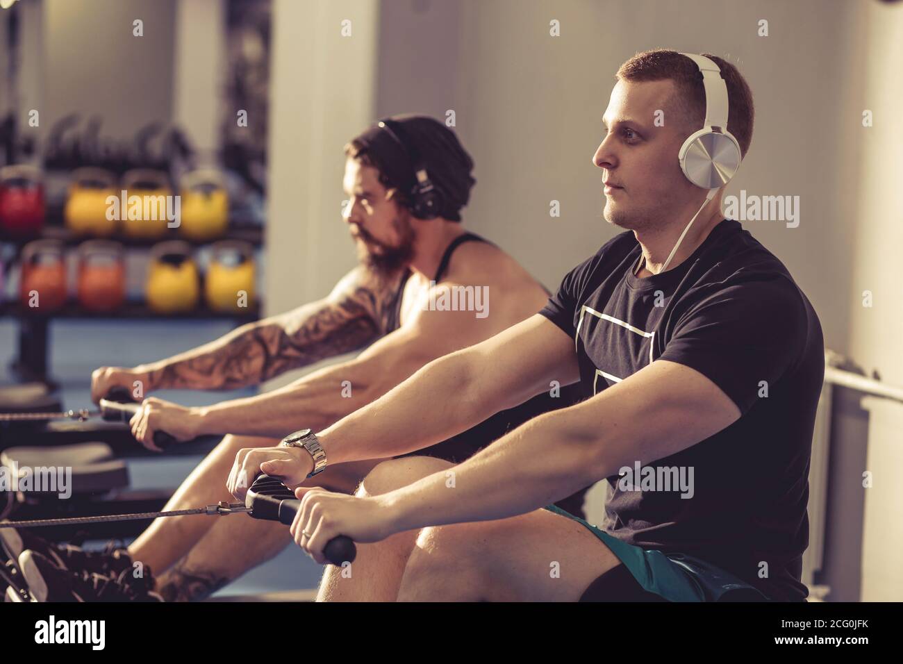 young sportsmen having hard workout on rowing machines in gym. Stock Photo