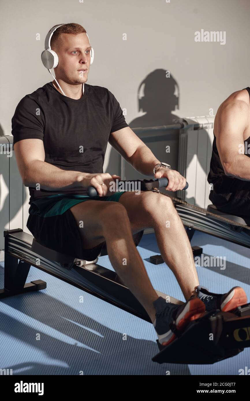 Side view of man and woman doing exercises with rowing machine at gym. Stock Photo