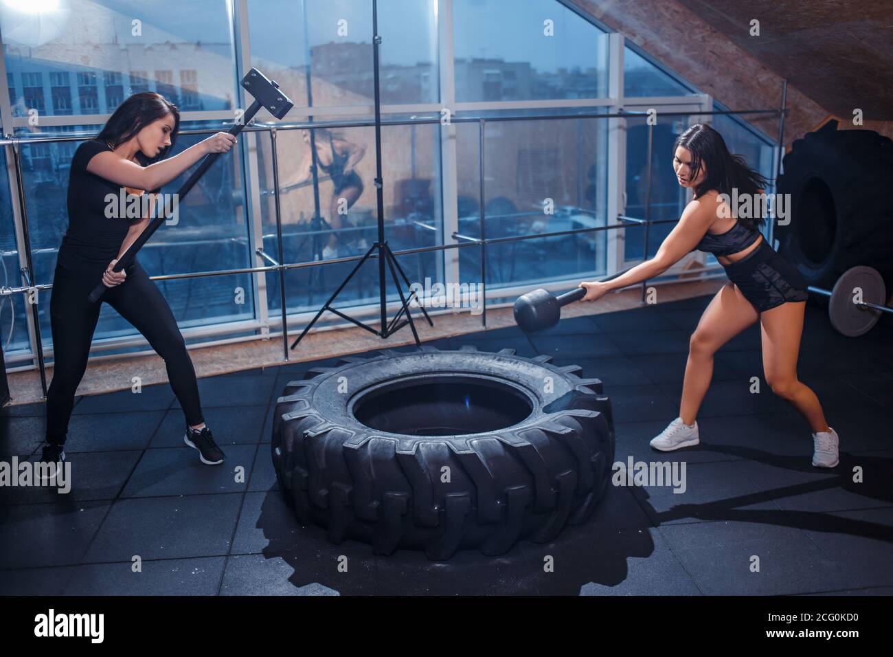 Female fitness model hitting a tractor tyre with hammer in a cross