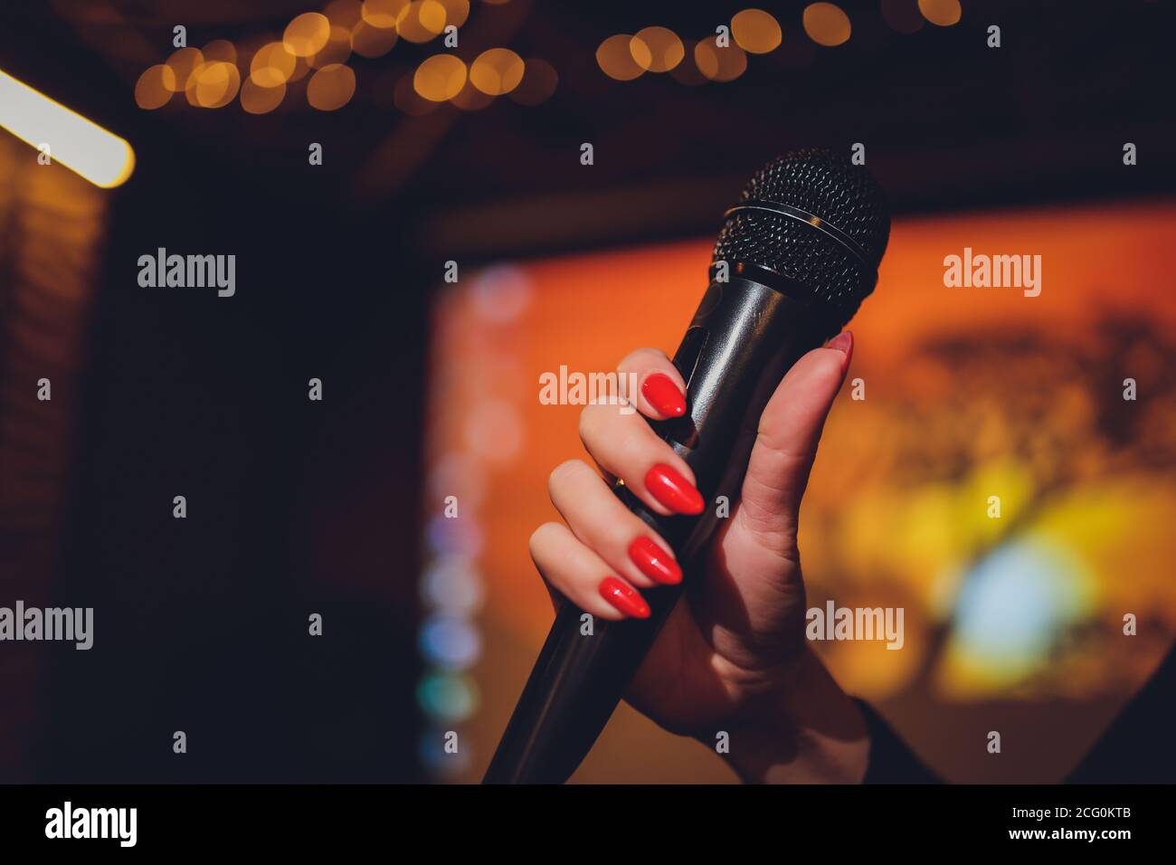 Microphone and female singer close up. Woman singing into a microphone, holding mic with hands. Stock Photo