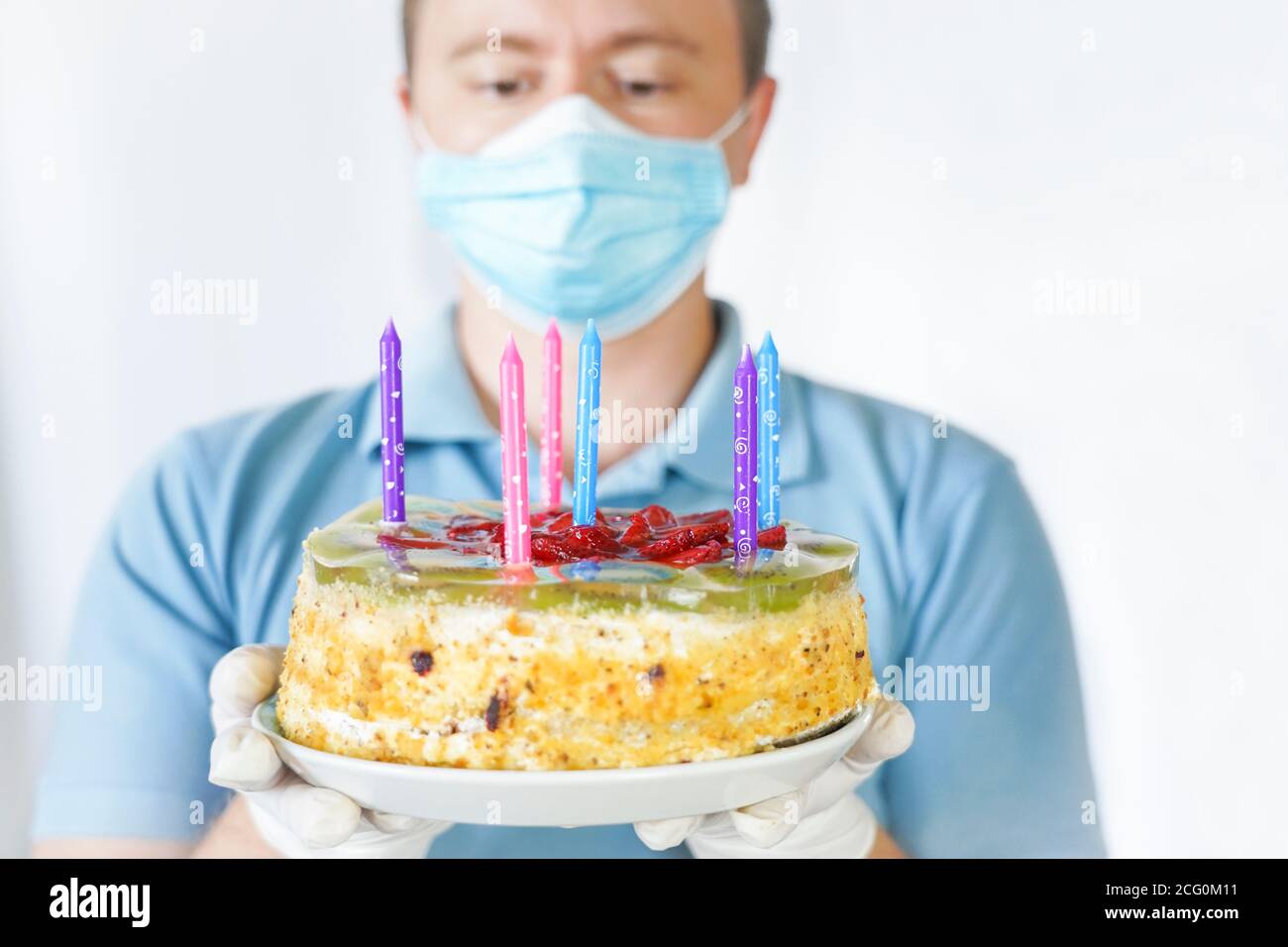 A guy in a mask and gloves holds a cake in his hand. Birthday celebration during covid-19 quarantine. Stock Photo
