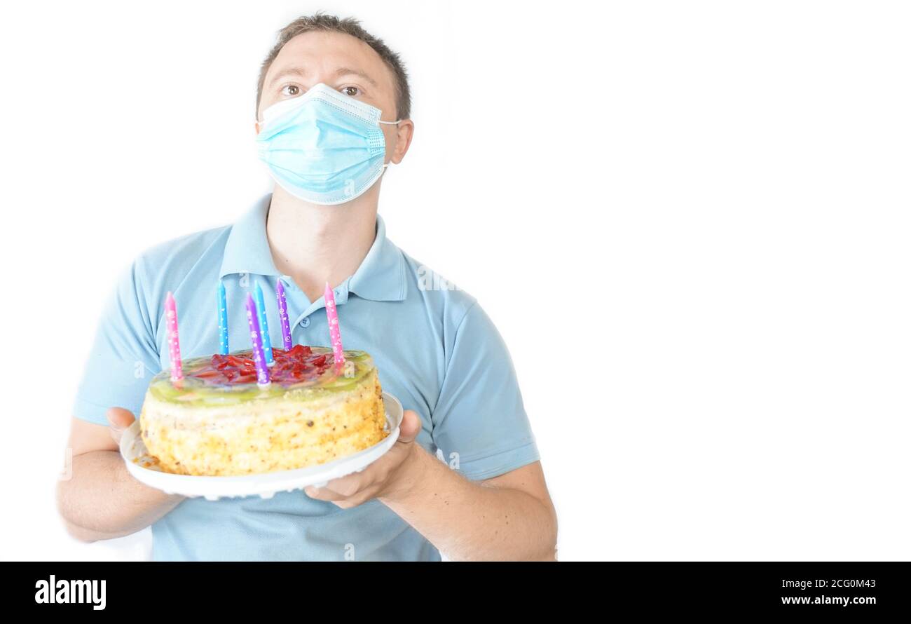 The guy in the mask holds a cake in his hand. Birthday celebration during covid-19 quarantine. White background Stock Photo
