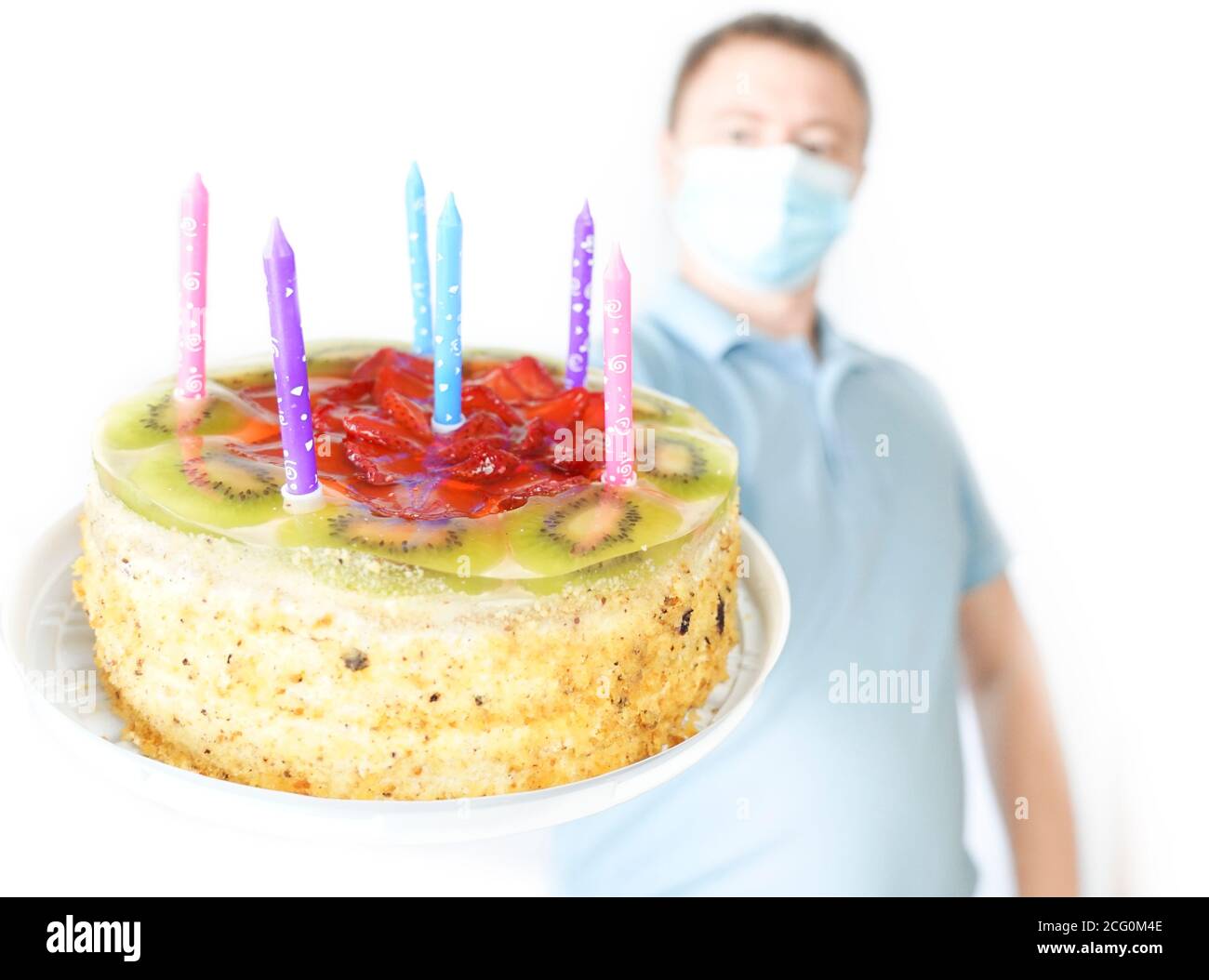 The guy in the mask holds a cake in his hand. Birthday celebration during quarantine covid-19 Stock Photo