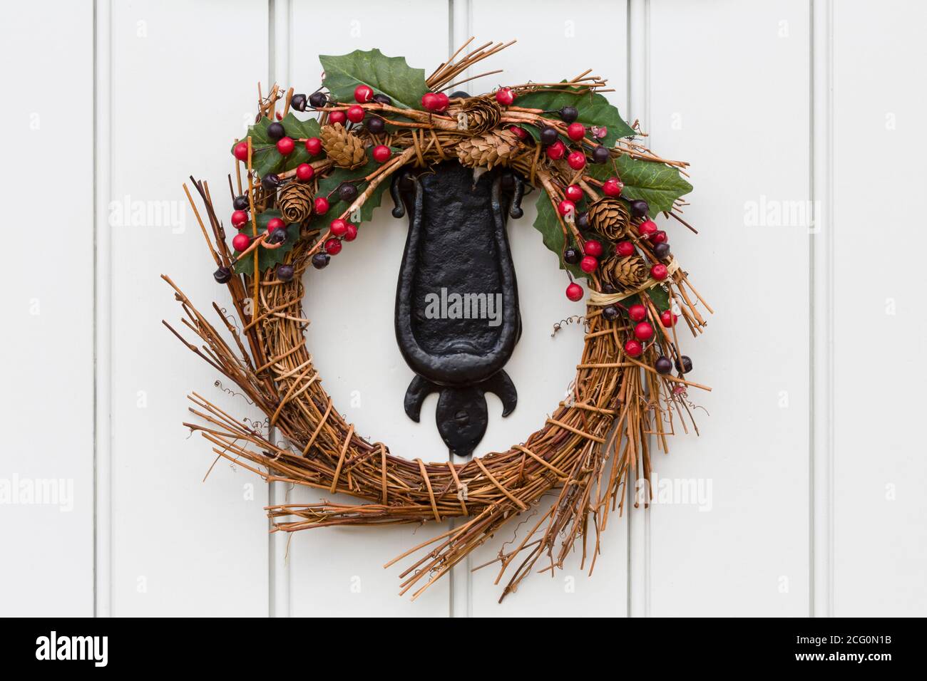 Detail of a Christmas wreath or garland on the cast iron knocker of a traditional painted wooden door Stock Photo