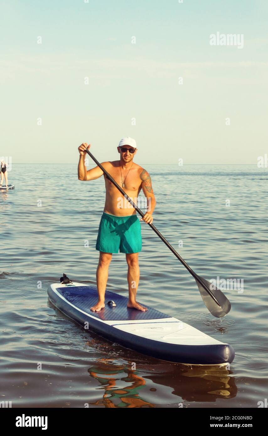 Young men is training on a SUP board in the summer sea. SAP Board surfing  Stock Photo - Alamy