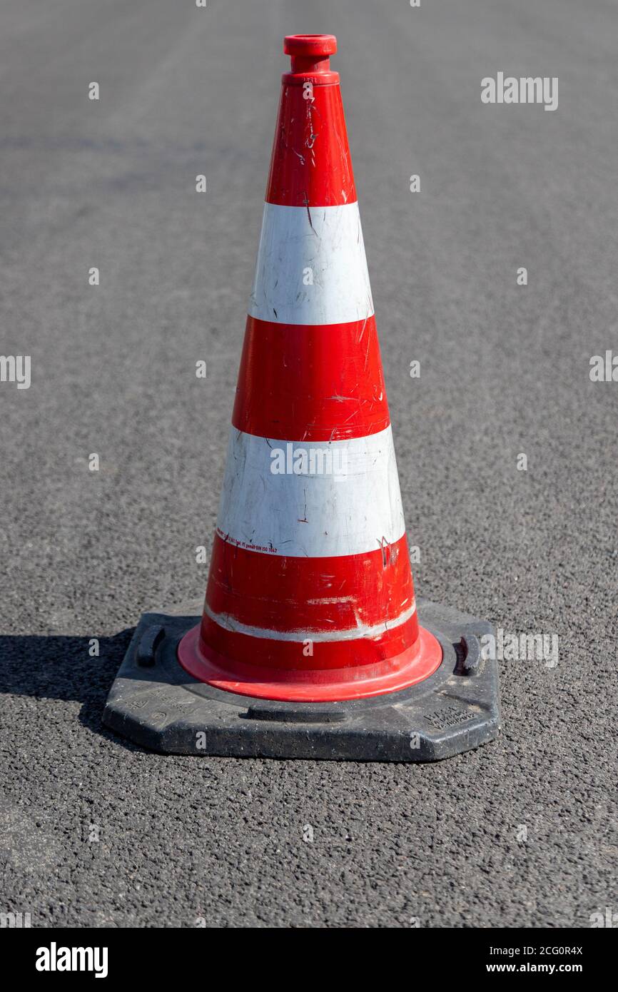A single red striped traffic cone, pylon, on asphalt, outdoors Stock Photo