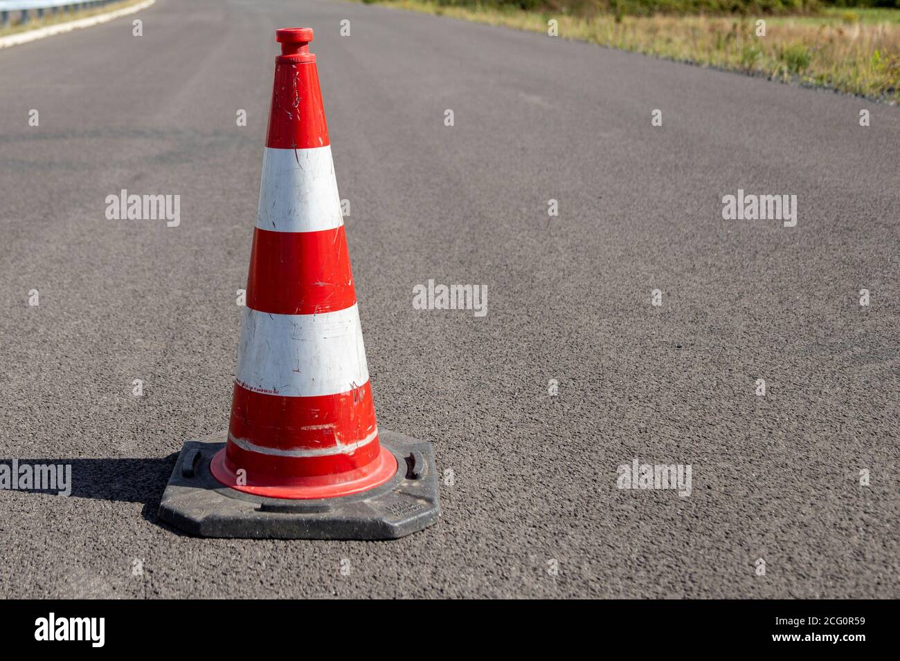 A single red striped traffic cone, pylon, on asphalt, outdoors Stock Photo