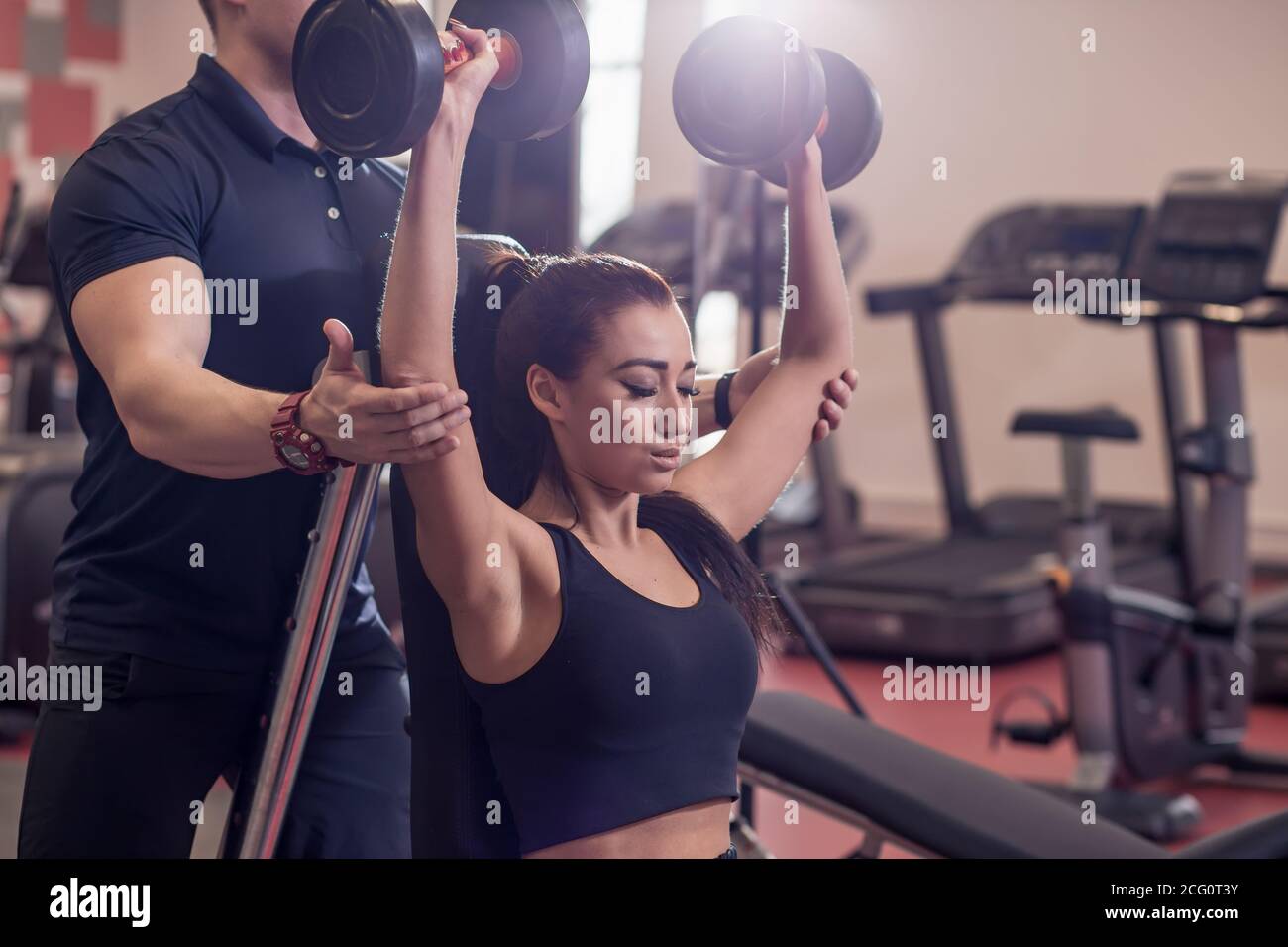 Woman with her personal fitness trainer in the gym exercising with ...