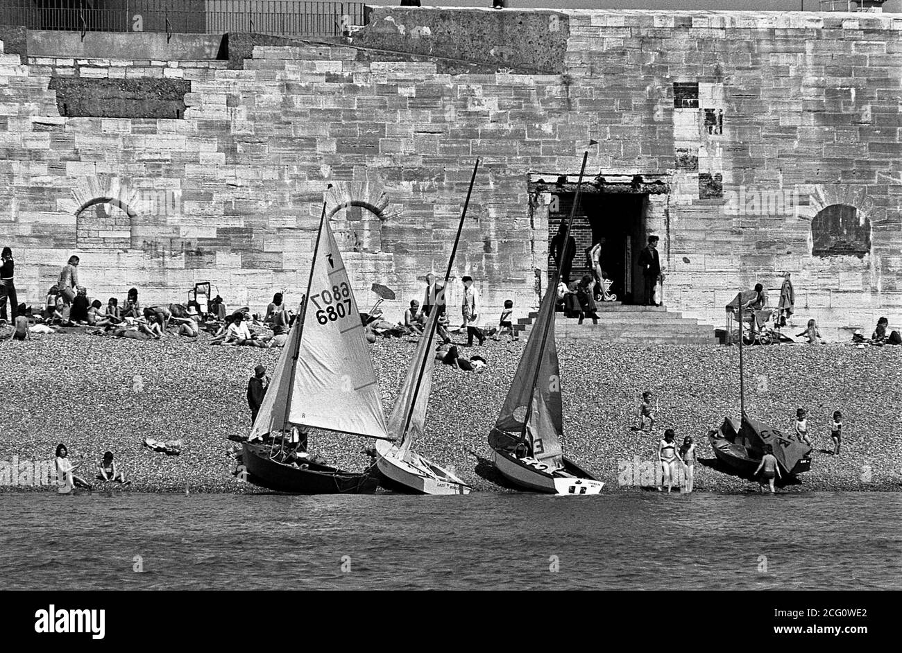 AJAXNETPHOTO. 1974. OLD PORTSMOUTH, UK. - HOT WALLS - PEOPLE RELAX ON THE STONY BEACH UNDER OLD PORTSMOUTH'S HOT WALLS, PART OF HENRY VIII'S FORTIFICATIONS BUILT TO DEFND THE TOWN IN THE 16TH CENTURY. IT WAS THROUGH THE HOLE (RIGHT CENTRE) CALLED SALLY PORT, VICE ADMIRAL HORATIO NELSON LAST SET FOOT ON ENGLISH SOIL BEFORE EMBARKING BY LAUNCH TO HMS VICTORY FOR IN SEPTEMBER 1805. PHOTO:JONATHAN EASTLAND/AJAX REF:741604 27 35 Stock Photo