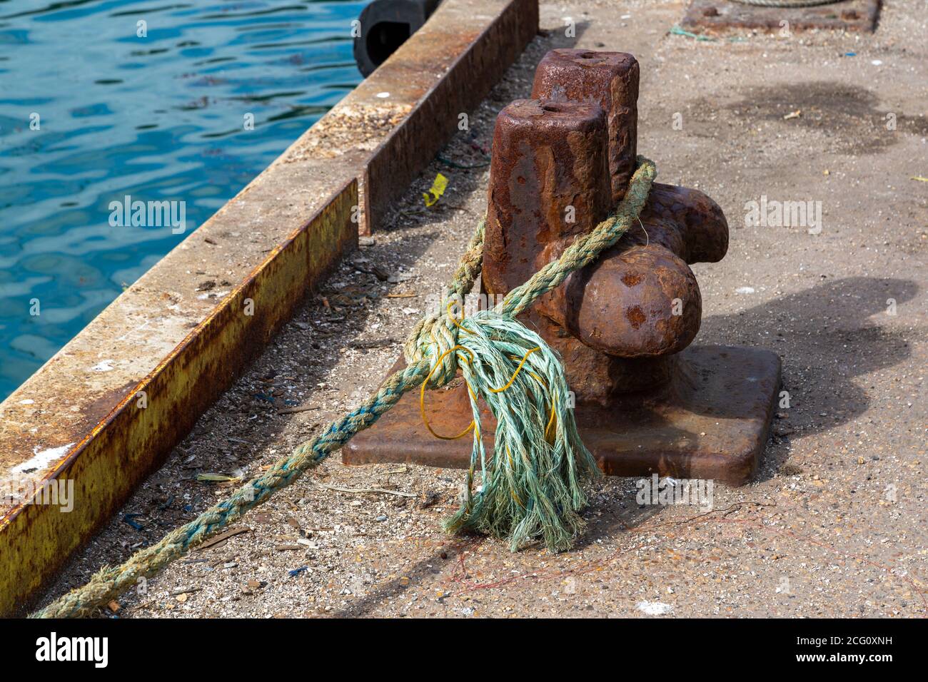 A bollard at a dockside with the rope of a boat tied around it to keep the boat moored to the jetty Stock Photo