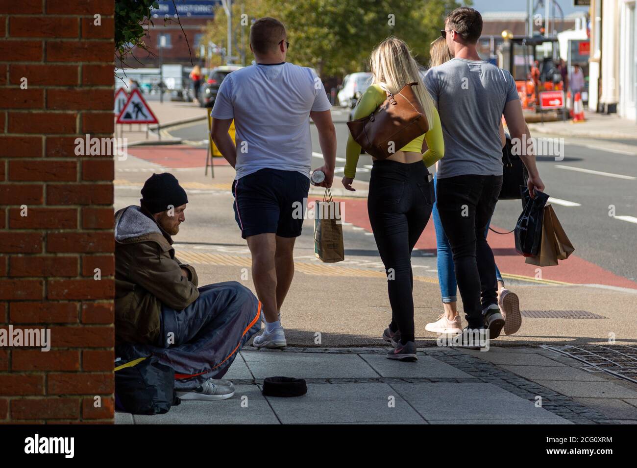 A group of young people walking past a homeless man begging in the street Stock Photo