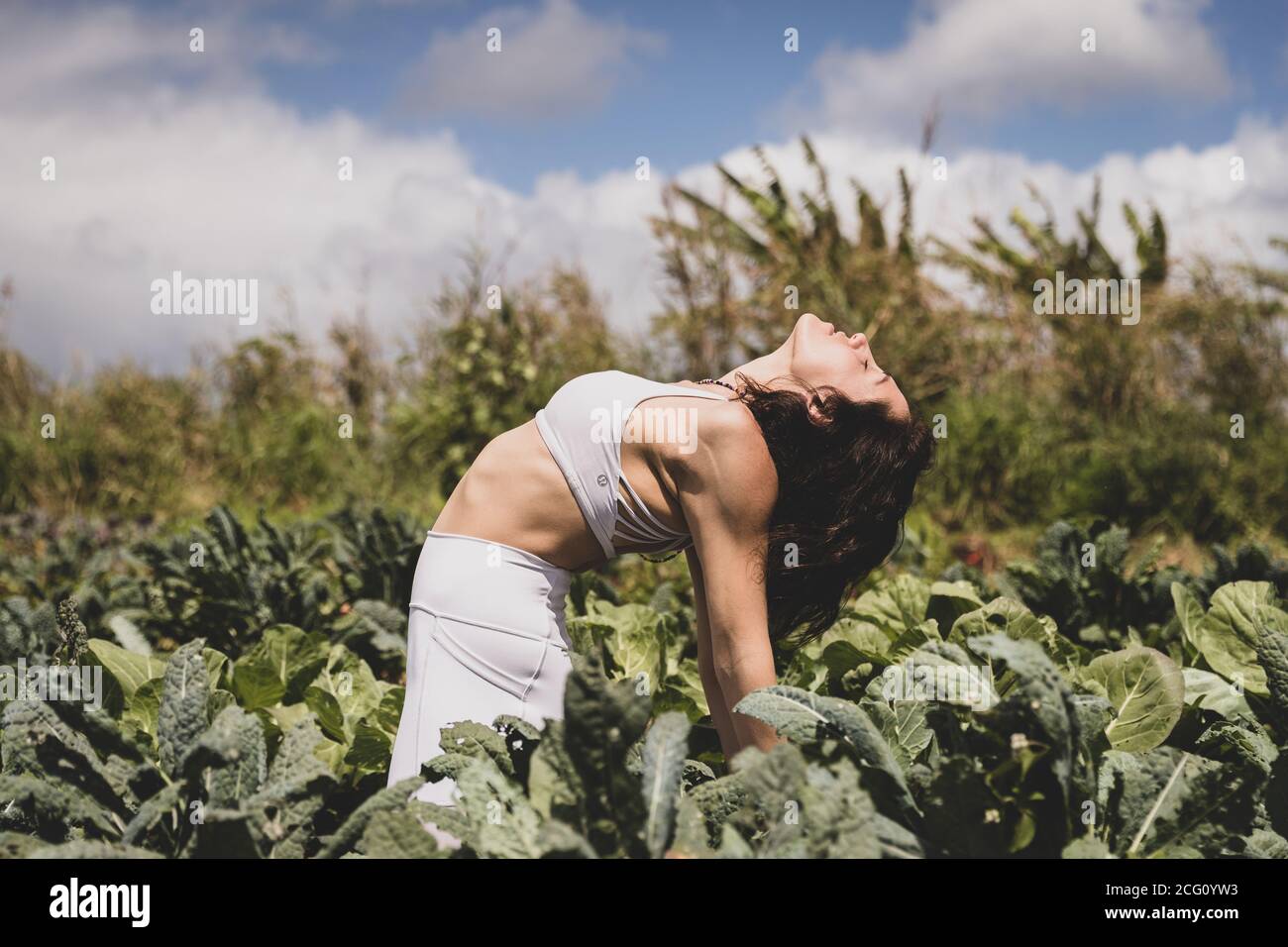 Female yogi backbends in field of vegetables Stock Photo