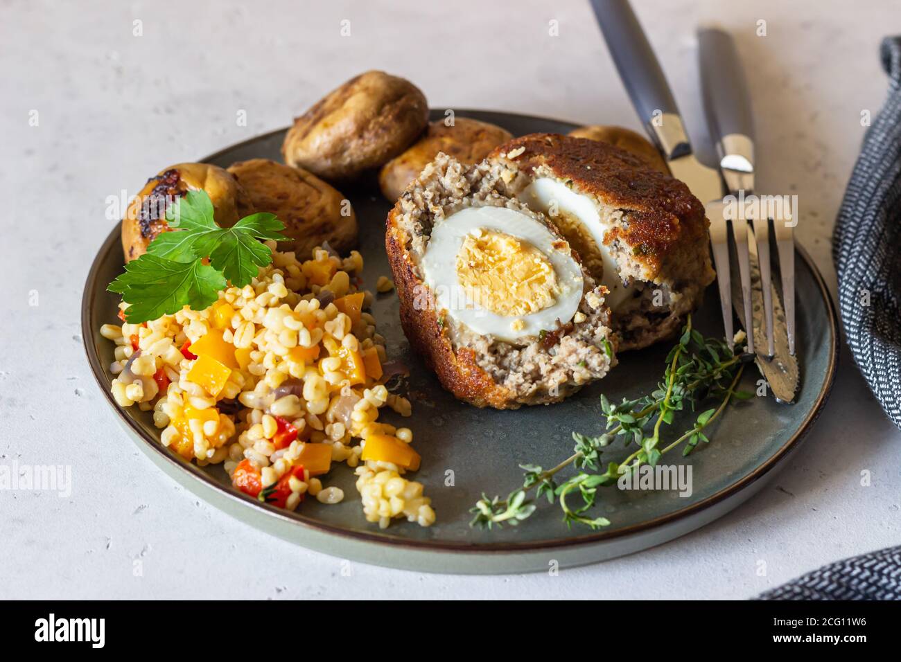Homemade scotch eggs on a ceramic plate served with bulgur pilaf, grilled mushroom and herbs. Meat cutlet with boiled egg. Traditional English cuisine Stock Photo